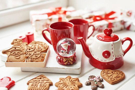 Christmas cookies and mug of hot tea, christmas time. Christmas gingerbread, candy, coffee in red cup on wooden table on frosty winter day window background. Home cozy holidays. Postcard Template.