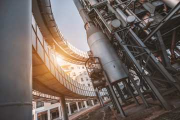 A wide-angle view from the bottom of a modern oil refinery or a contemporary fuel factory facility in an industrial zone, two round bridges, pipes, beams, tanks, an auxiliary building behind