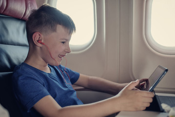 Comfortable flight. Happy European boy watching movie sitting at airplane while flying during his...