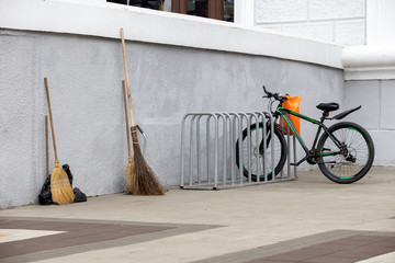 brooms and scoops against the wall and a parked black bike in a bicycle park