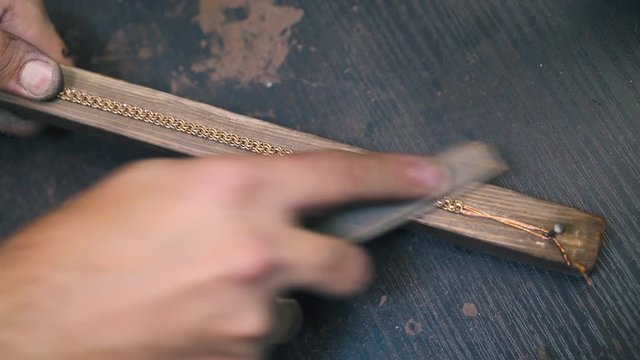 CU shot: young jeweler grinds new golden bracelet with rasp on wooden gutter at dark table in workshop close view