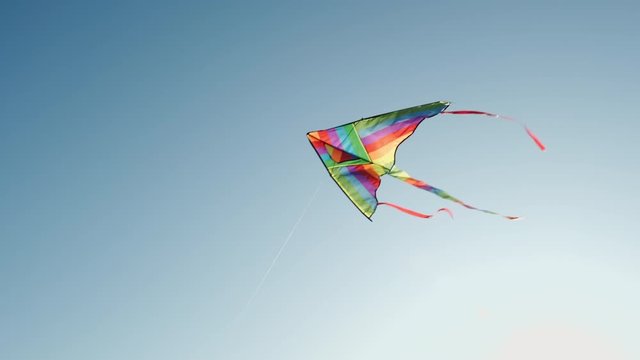 Colored kite with an emoji hangs in the air against a blue sky on a sunny summer day at a city kite festival. The tail of a kite sways in the wind. Children's 