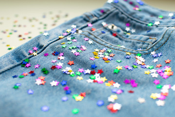 Festive colorful confetti scattered at light blue jeans. Close up of jeans decoration tiny shining...