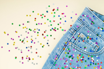 Party preparation flat lay. Festive colorful confetti as tiny colorful stars scattered at light blue mom jeans and ivory background. Jeans decoration. Modern fashion. Festive decoration.