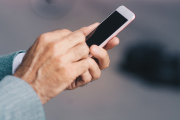 Senior businessman holding a cellphone. The focus is on the hands and the phone.