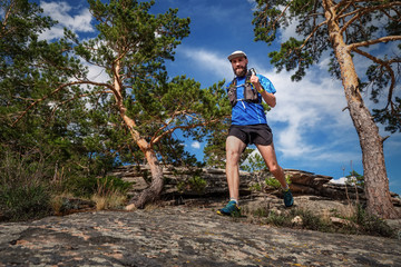 Male runner running on a mountain trail. Man in blue jersey and black shorts training outdoors on a sunny day