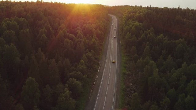 Yellow hatchback fast driving in winding asphalt road in dense forest hilly landscape / Summer sunset - Aerial drone view