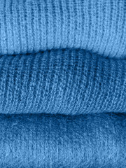 Pile of cozy winter woolen sweaters in classic blue color of 2020