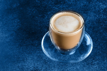 A cup of coffee in glass cup on blue dark background table. Copy space. Morning Drink Cappuccino