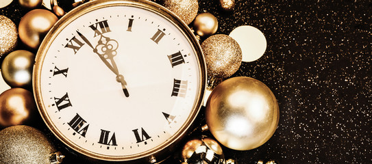 Gold vintage clock decorated with christmas balls on a black background in sparkles. Twelve...