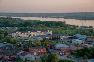 Fototapeta na wymiar Small town with tiny houses near the river and green forests and fields. Trees and their shadows on the grass. Sundown and sunrises. View from high on the landscape