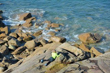 A young boy who is sitted on a rock at the seaside