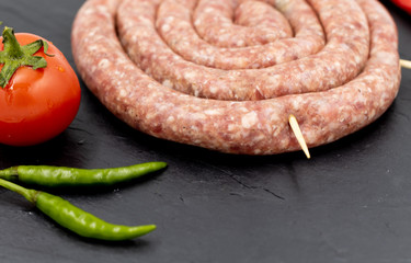 Raw sausage on a black background. Decorated with tomato and chili pepper.