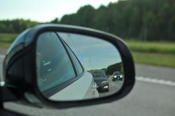 A rear view mirror of a car with pine forest in background