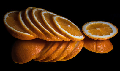Fresh organic orange fruit, sliced, with reflection on shiny black background
