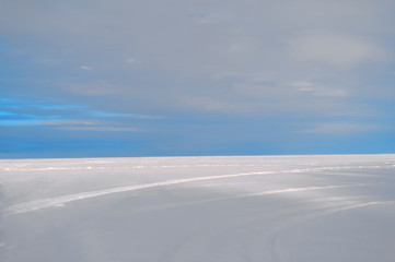 Path under a turquoise sky through a snowy field. The horizon between the sky and the snow field divides the frame in a ratio of one to four. You can place the text top.