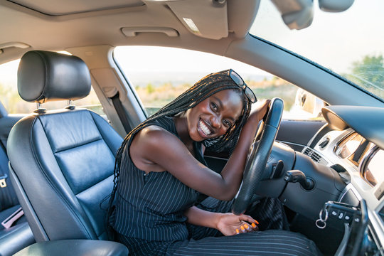 Happy smiling african girl in black striped clothes is driving a car