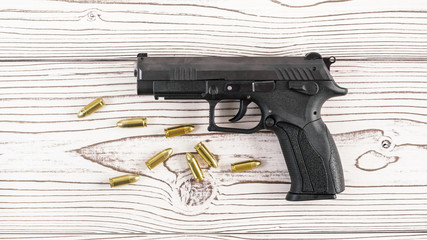 Fototapeta premium Simple black modern pistol gun with few yellow brass bullets on white wooden board, view from above
