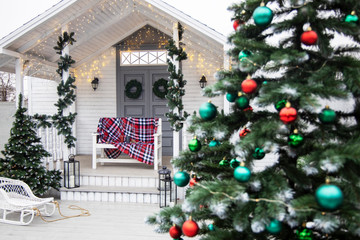 Winter exterior of a country house with American-style Christmas decorations. Snow covered courtyard with porch, tree and wooden vintage sleigh.