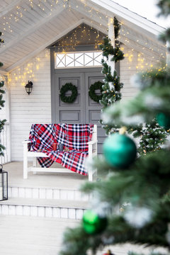 Winter exterior of a country house with American-style Christmas decorations. Snow covered courtyard with porch, tree and wooden vintage sleigh.