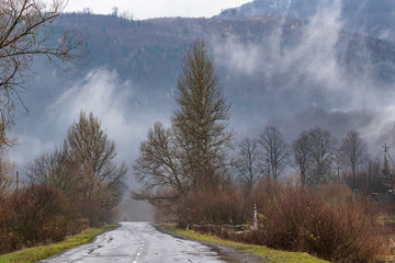 Deserted road in the mountains. The tops of high mountains are hidden by clouds. Fog. Autumn landscape. Panoramic view.
