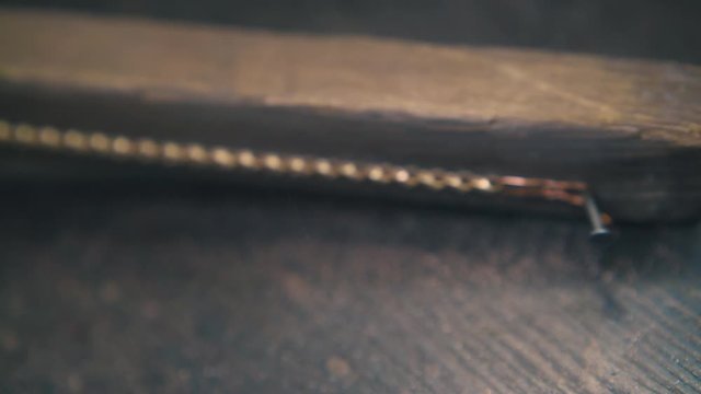 CU shot: young jeweler polishes shining gold chain with rasp on wooden gutter at dark table in workshop extreme closeup