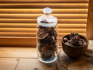 Wooden Cup and glass with a cone and walnuts on the windowsill. Wooden blinds.