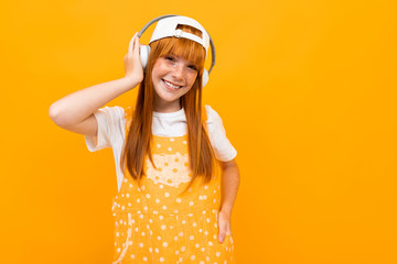 smiling red-haired girl listens to music on headphones on a yellow background.