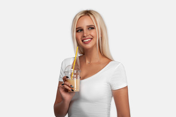 Funny cute attractive careless blonde woman is drinking cocktail in a plastic cup using a straw, isolated on white background. So delicious. Sexy smiling girl with juice.