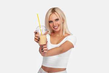 Funny cute attractive careless blonde woman is drinking cocktail in a plastic cup using a straw, isolated on white background. So delicious. Sexy smiling girl with juice.