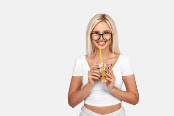 Funny cute attractive careless blonde woman is drinking cocktail in a plastic cup using a straw, isolated on white background. So delicious. Sexy smiling girl with juice.