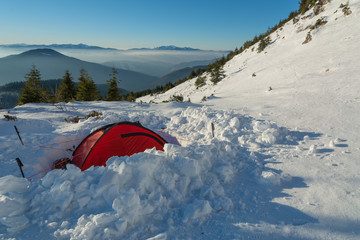 Winter camping high in the mountains, among the clouds and fog in the red tourist tent.