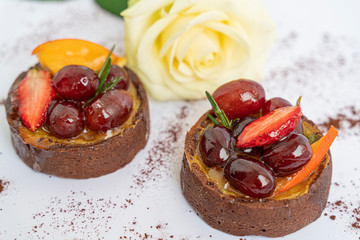 Two tasty chocolate cakes with icing fruits and berries on white background with white rose, isolated and close up