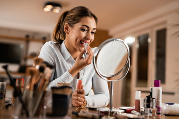 Beautiful woman using lipstick while looking herself in a mirror.