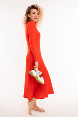 pretty curly girl in a red dress holds shoes in full growth on a white wall