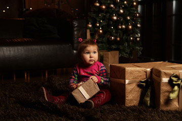 Fototapeta na wymiar a small, beautiful girl, receives gifts for Christmas,and makes a wish near the Christmas tree