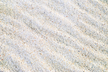 Sand rippled by the sea sparkles with bright chips of seashell.