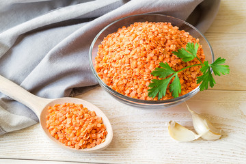 Dried red lentils in a glass bowl and in wooden spoon on on white rustic table. Ingredients for vegetarian puree soup. Healthy eating and vegan food.