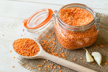 Dried red lentils in a glass clip top jar and wooden spoon on sackcloth table napkin over white rustic table. Ingredients for vegetarian puree soup. Healthy eating and vegan food.