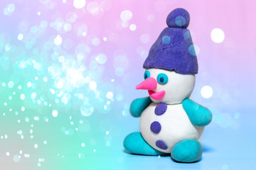 white plasticine snowman with purple winter hat, pink nose, playdough or modeling compound dough, blurred christmas neon background, blue bokeh lights, concept of festive atmosphere of holiday