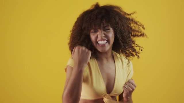 Young beautiful brunette curly hair girl happily rejoicing saying yes on yellow backgroundin slowmotion. Success and achievement concept. Cheerful pretty woman on yellow background. Cinematic 4k.