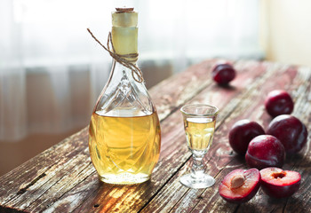 A bottle of traditional Balkan plum brandy - rakija or rakia slivovica near a wineglass with sljivovica and fresh plums on the old wooden background in dayligt.