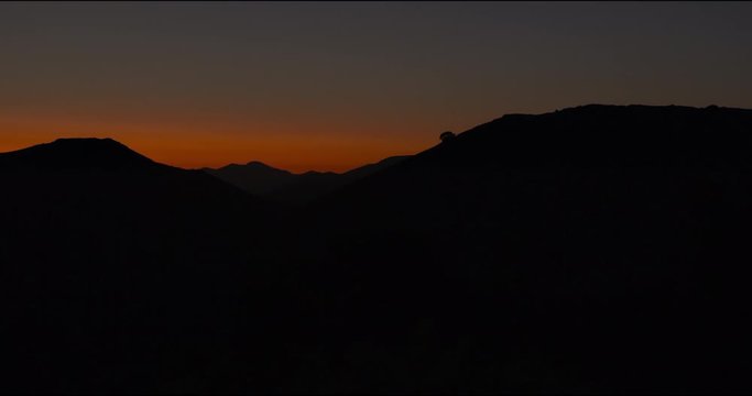 Pan right to left, mountains behind tree silhouettes, shot against the sunset, burning red sky.