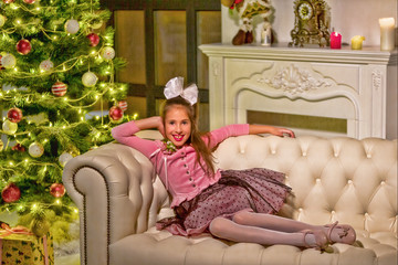 Beautiful little girl sitting on a sofa near the New Year tree.