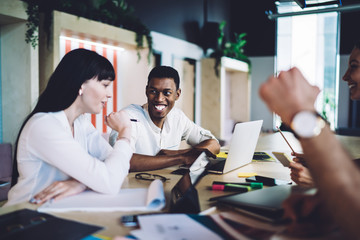 Diligent multiracial colleagues discussing project and surfing laptop during meeting