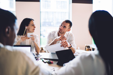 Confident colleagues having conversation and holding papers during meeting