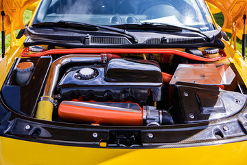Yellow small Car under hood showing high performance engine tuning and modification, red, silver, chrome and carbon fiber clean parts