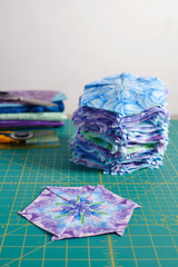 Stacks of hexagonal patchwork blocks, quilting accessories on a cutting mat