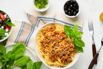 Dining table concept. Spaghetti with Bolognese sauce, vegetable and greens salad with olives, Parmesan cheese and spices