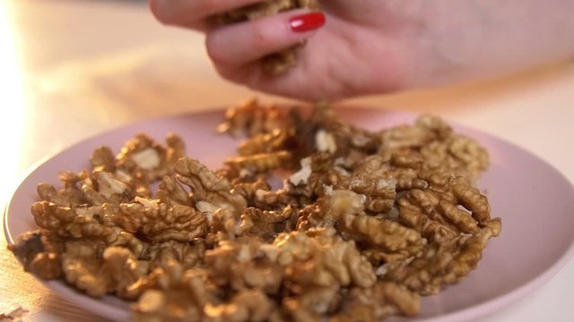 Woman collects peeled Walnuts and drops them into pink plate